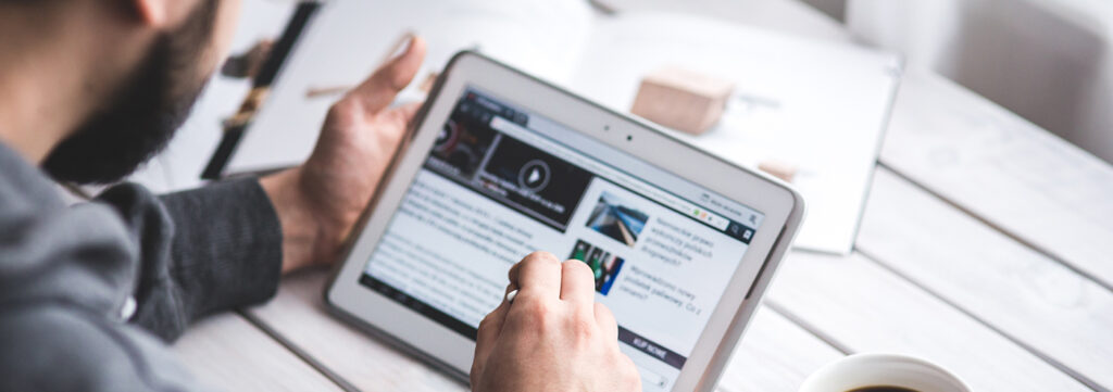Person reading news on a tablet with a coffee nearby