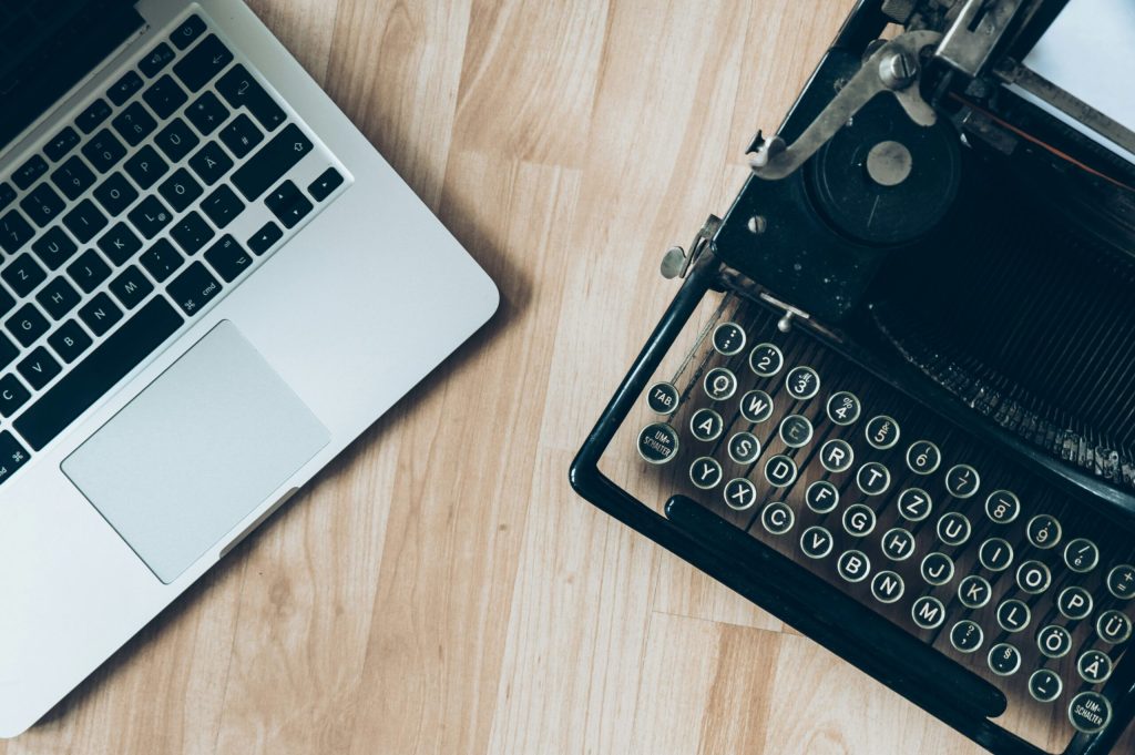 A modern laptop next to an old typewriter, contrasting old and new technology