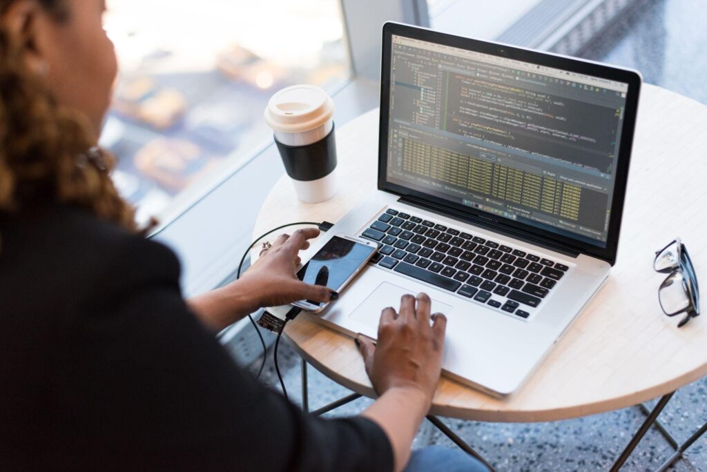 Blog 1 - In Content 2 Woman connecting a smartphone to a laptop displaying code