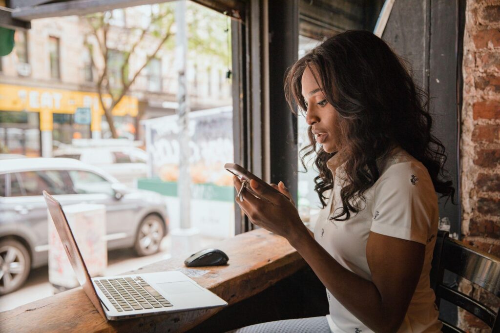 Woman using her personal phone next to a work laptop in a cafe